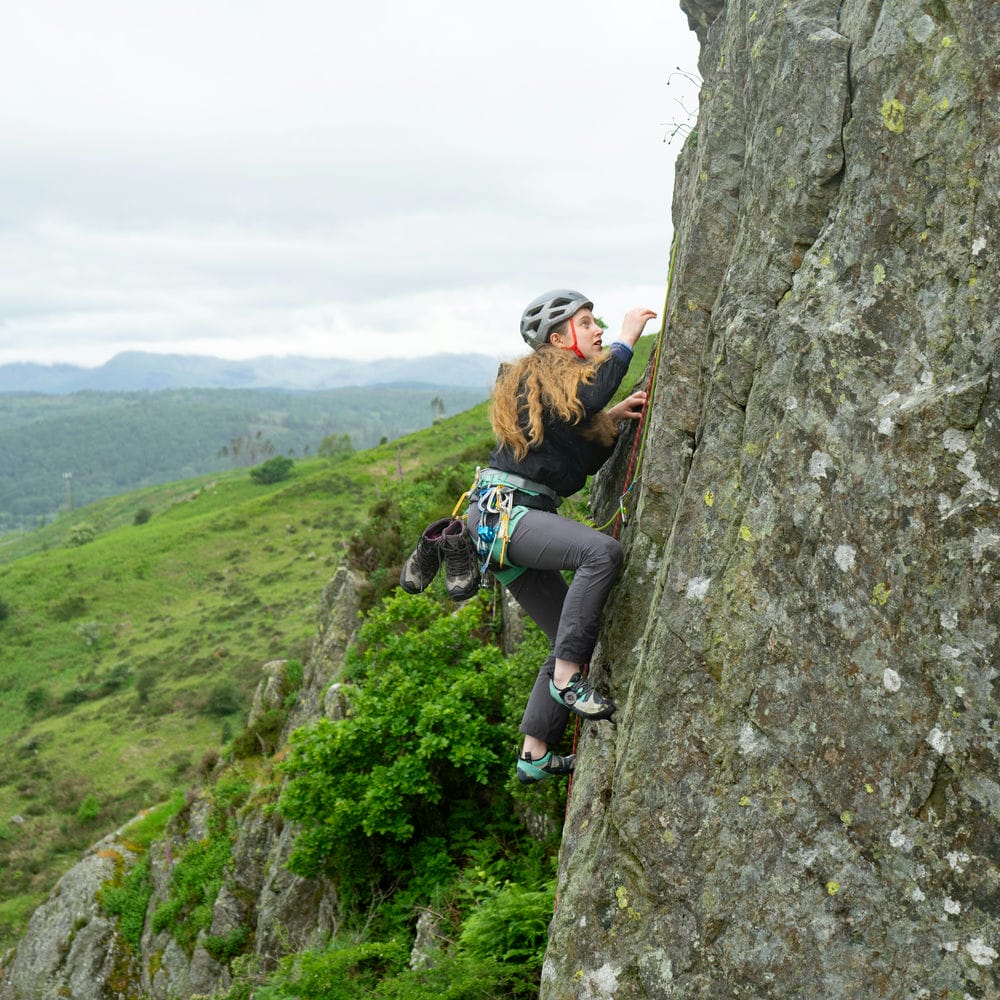 side shot of someone climbing outside who is being guided up by an instructor