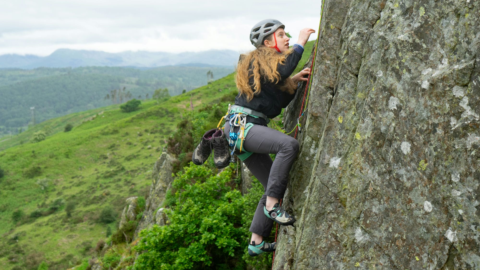 wide shot of someone climbing outside who is being guided up by an instructor showing the mountains of the lake district in the background