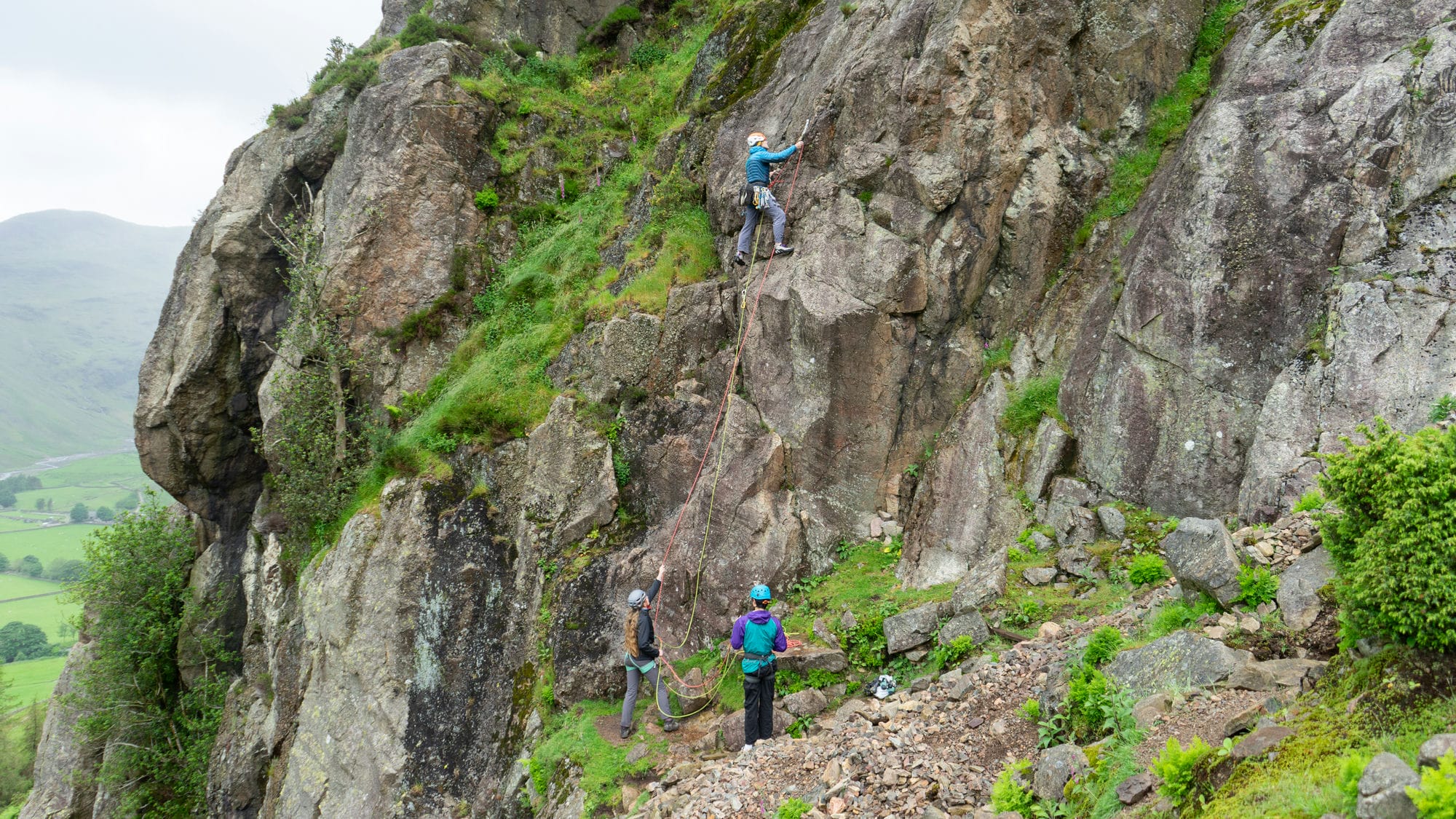 person setting off to lead a traditional rock climb with two clients belaying them